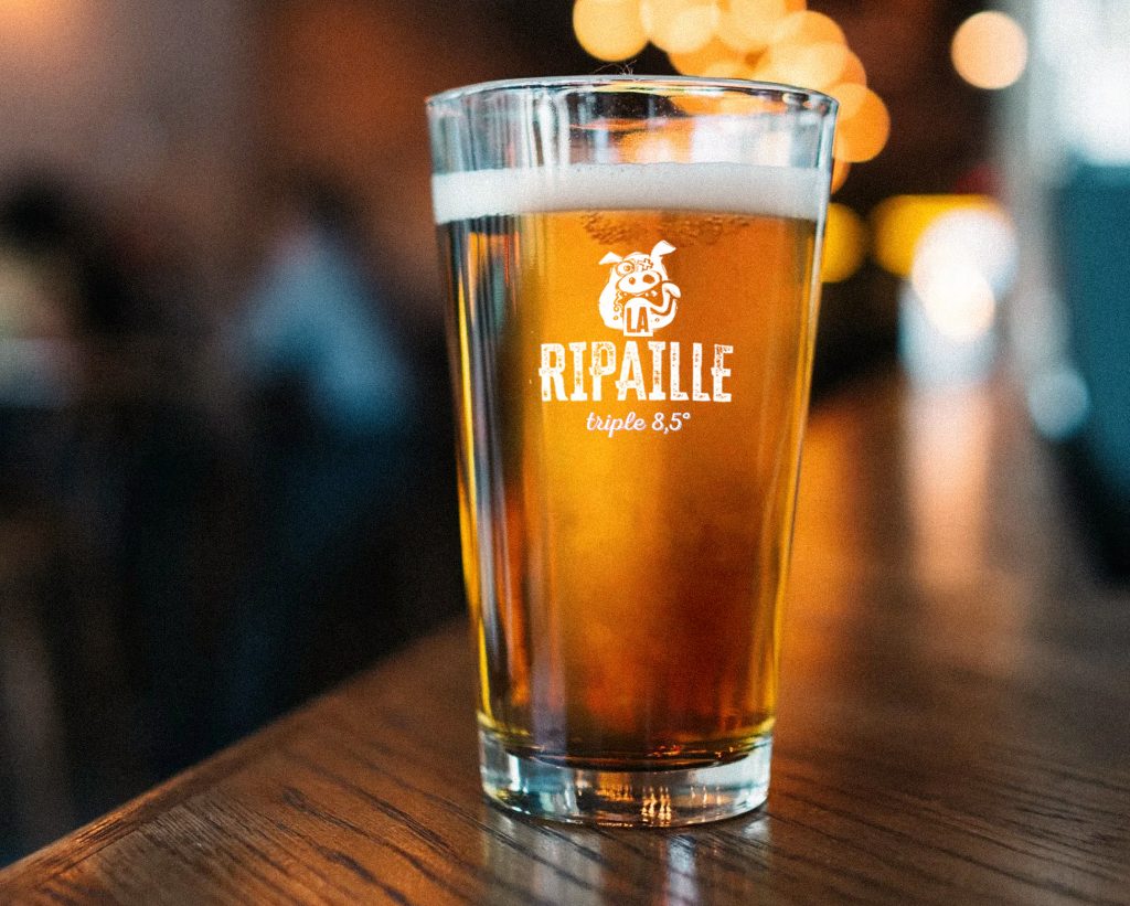Photomontage du verre de bière Goz dans une ambiance de bar, mettant en valeur le design du verre et l’identité de la marque, créant une atmosphère conviviale et authentique.